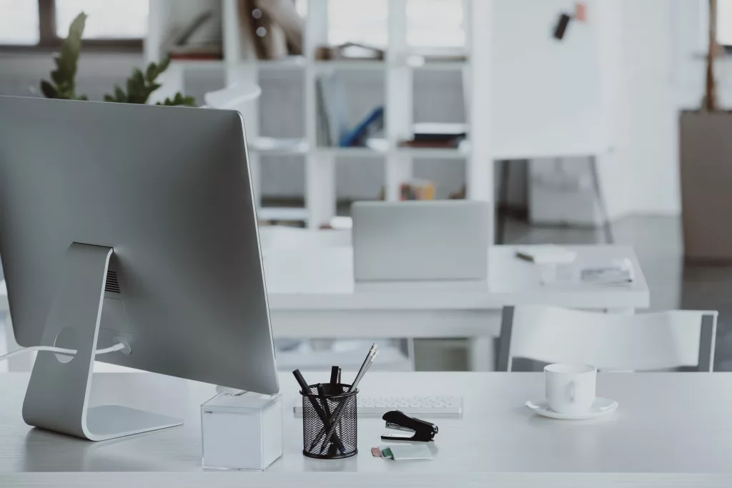 "Modern office workspace with a desktop computer, stationery, coffee cup, and shelves in the background."
