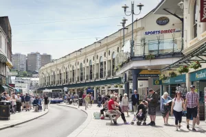 Busy shopping street in Torquay with people walking, sitting, and shopping outside Fleet Walk, with visible shops including Poundland and Sports Direct